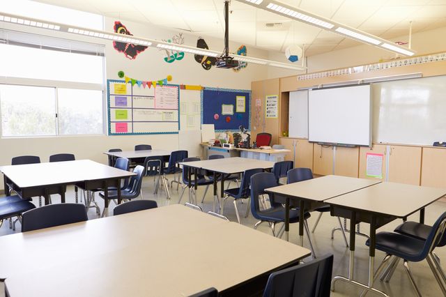 an empty classroom full of desks, a teacher's desk, and screen